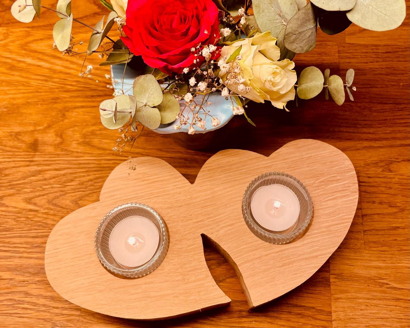 Zwei Holzherzen mit Kerzenhaltern, umgeben von einer Blumenarrangement.